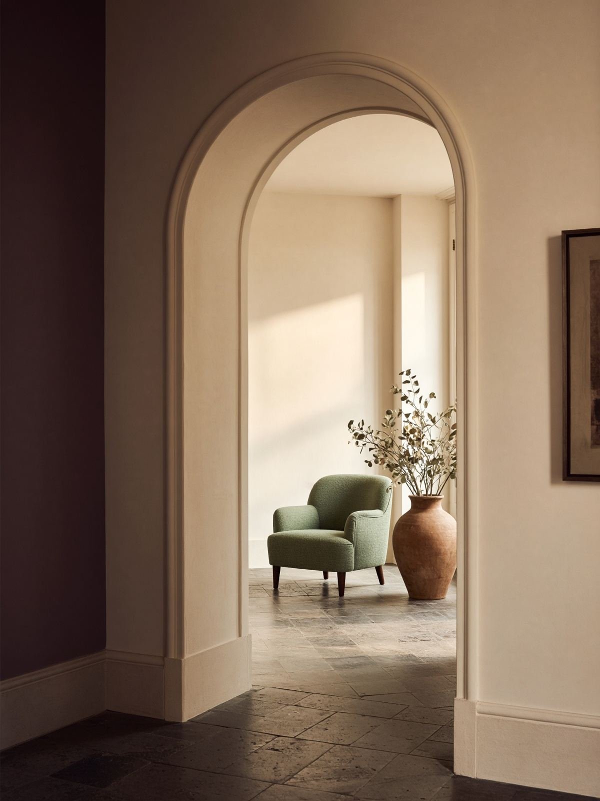 An arched doorway opening into a bright room with a sage chair.